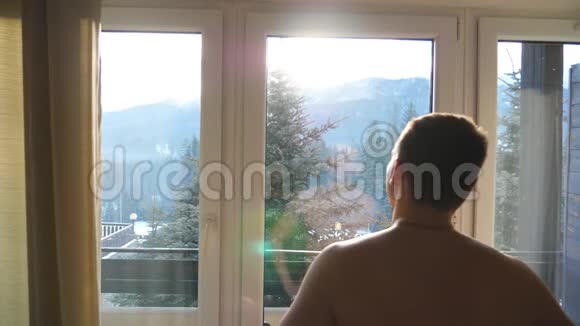 在一个阳光明媚的日子里一个面目全非的运动员站在酒店的卧室里向窗外望去帅哥视频的预览图