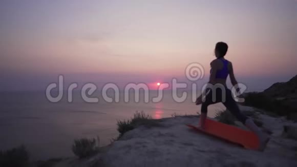 4K瑜伽站在海洋上方的悬崖上一个穿着漂亮迷人的女孩举起双手飞向天空站在瑜伽里视频的预览图
