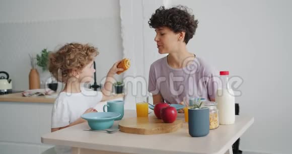 小男孩用牛角面包喂妈妈然后在家吃早餐时喝酒视频的预览图