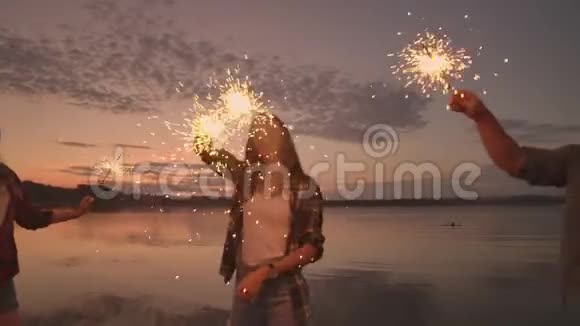 一群男人和女人的朋友在海滩上用火花和烟花庆祝节日慢动作视频的预览图
