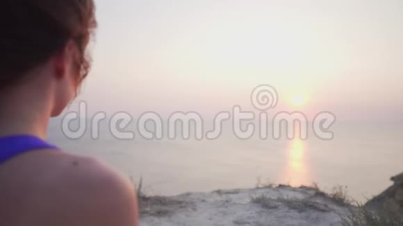 一个穿着运动服的女人正在冥想一边看着海洋上的日落从后面看视频的预览图