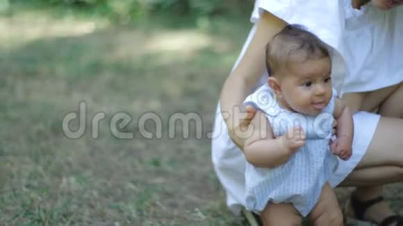 年轻漂亮的母亲穿着一件白色的衣服教她刚出生的女儿在公园里的一片新鲜的绿草上行走母亲和视频的预览图