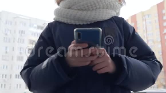 青少年女孩在冬天散步时使用手机将手持智能手机的少年女孩举在住宅的冬季街道上视频的预览图