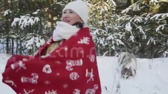 微笑的女人裹着圣诞格子在雪地森林里和狗在冬天散步穿着红色格子衣服的快乐女人视频的预览图