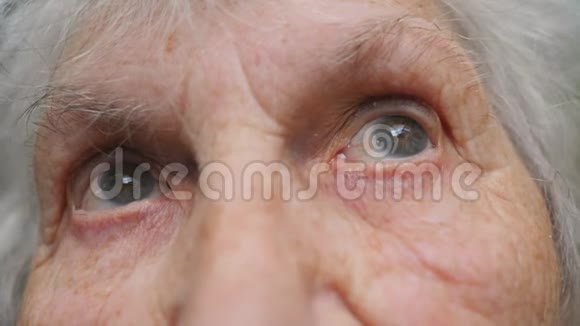 老妇人的眼睛从一边移动到另一边然后看着镜头一位长着皱纹的老太太的眼睛视频的预览图