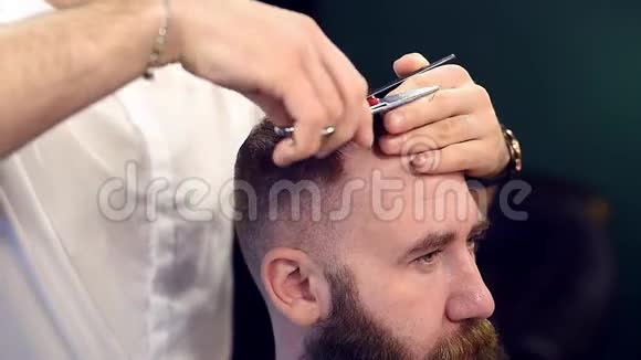 客户背后的理发师用手指剪刀在前锁上剪头发剪头的留胡子男人的侧视视频的预览图