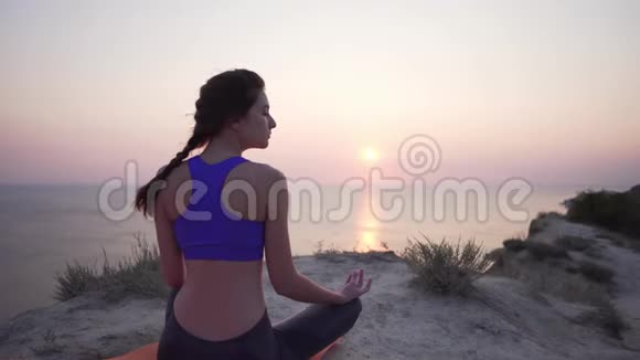 美丽而平静的年轻女孩闭着眼睛练习瑜伽从后面看一个静态的景色早上在海边视频的预览图