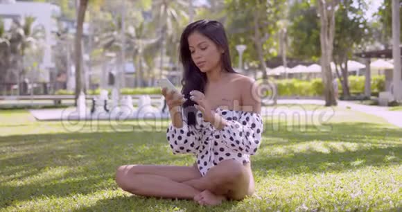 穿着现代泳装坐在公园里的智能手机微笑的亚洲女人视频的预览图