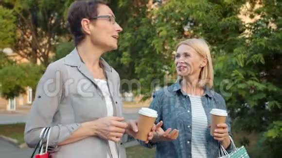 快乐的朋友在公园里散步笑着拿着咖啡和袋子视频的预览图