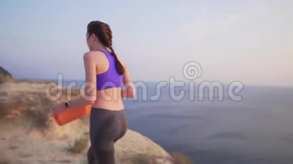 苗条的女孩在悬崖旁边有一块地毯用来做运动或瑜伽日落或大海边的黎明视频的预览图