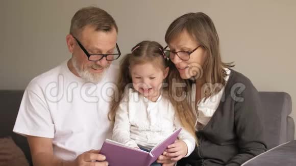 可爱的祖父母和他们的孙子坐在书上一起读有趣的故事的画像视频的预览图