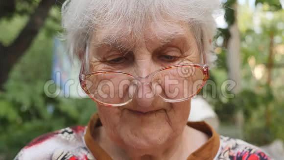 戴眼镜的老妇人看着相机微笑着在户外戴眼镜的幸福奶奶的画像视频的预览图