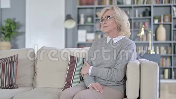 疲惫的老妇人坐在沙发上背痛视频的预览图