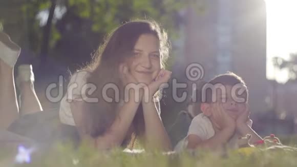 户外姐姐和弟弟的肖像那个男孩和女孩一起躺在公园的草地上看着视频的预览图