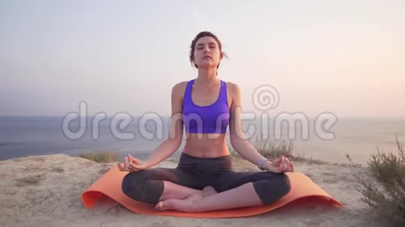 一个漂亮的女孩坐在莲花的位置举起双手在自己上方做瑜伽有魅力的女运动员视频的预览图