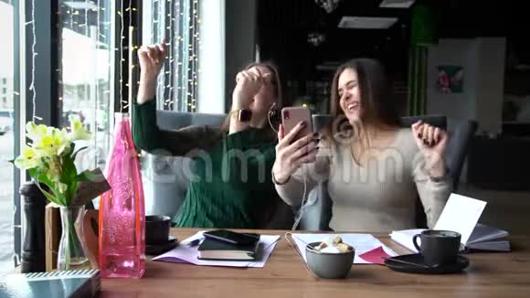 两个快乐的年轻女孩朋友坐在咖啡桌旁一起玩得很开心视频的预览图