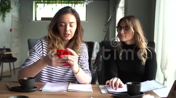 年轻开朗的女孩最好的朋友正坐在咖啡馆里用智能手机笑着视频的预览图