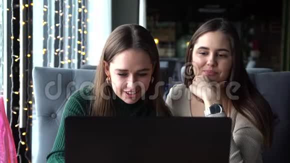 两个情绪积极可爱的可爱朋友吃午饭坐在咖啡馆里用笔记本电脑视频的预览图