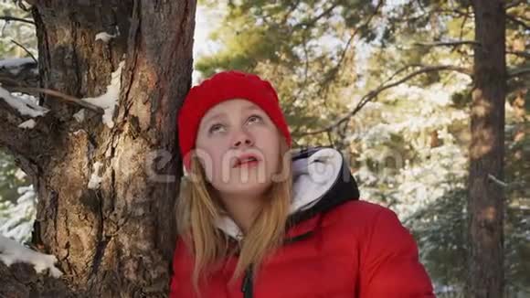 在白雪皑皑的森林里穿着红色帽子和外套的年轻女子肖像近脸少女看着视频的预览图