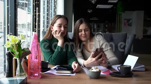 两个女人白天坐在咖啡馆里一起在智能手机上看视频视频的预览图
