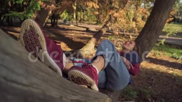 穿运动鞋的女孩在傍晚的阳光下在公园的一棵树上休息把注意力集中在运动鞋上女孩迷离了视频的预览图