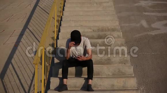 年轻的现代人没有鞋子坐在城市楼梯上使用智能手机戴着黑色的帽子和袜子视频的预览图
