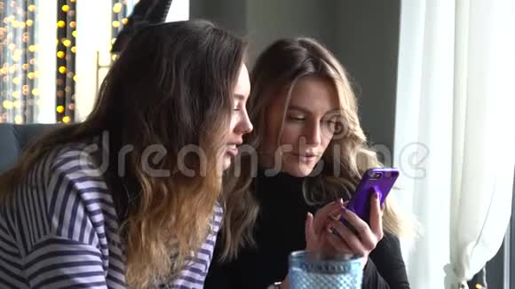 两个女朋友坐在咖啡馆里用手机看照片视频的预览图