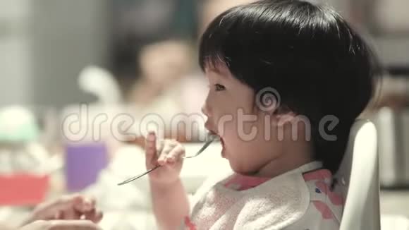 亚洲蹒跚学步的小女孩和妈妈一起吃零食的肖像妈妈帮助她自己用餐叉和餐桌气氛视频的预览图