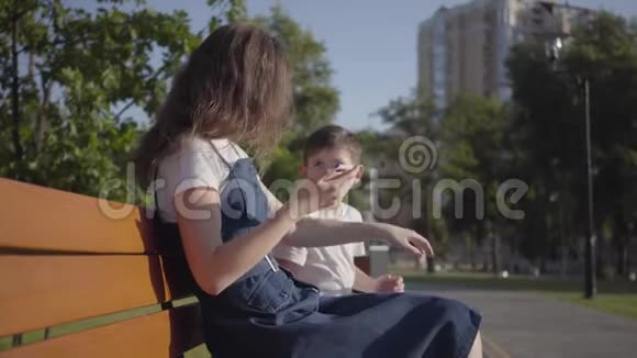 姐姐和弟弟坐在夏天公园的长凳上那个男孩试图带走但没有成功视频的预览图