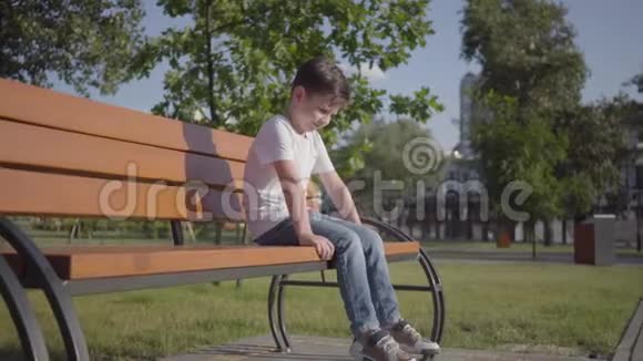 悲伤孤独的小男孩坐在公园的长凳上可爱的孩子独自呆在户外夏日休闲视频的预览图