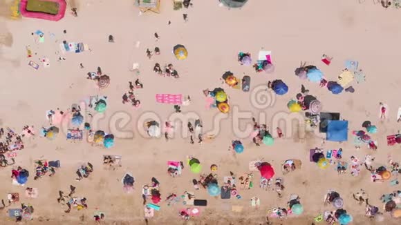 在炎热的夏日带着五颜六色的雨伞和人4K海滩的俯视图视频的预览图