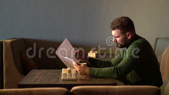 年轻迷人的留胡子的时髦男人坐在咖啡馆里读文件视频的预览图
