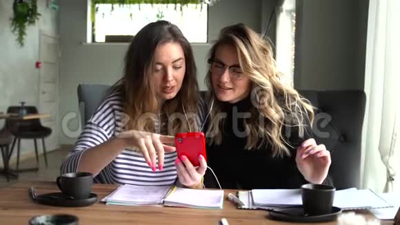 两个女人白天坐在咖啡馆里一起在智能手机上看视频视频的预览图