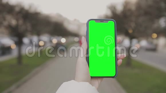 女孩拿着绿色屏幕模糊的城市背景手机视频的预览图
