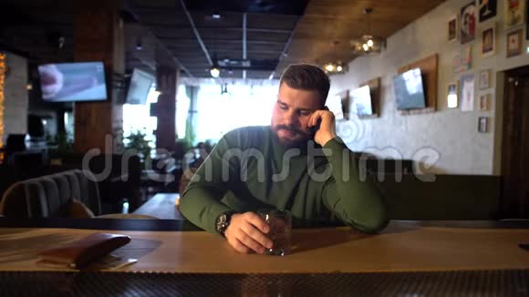 一个留胡子的男人坐在酒吧喝威士忌打电话视频的预览图