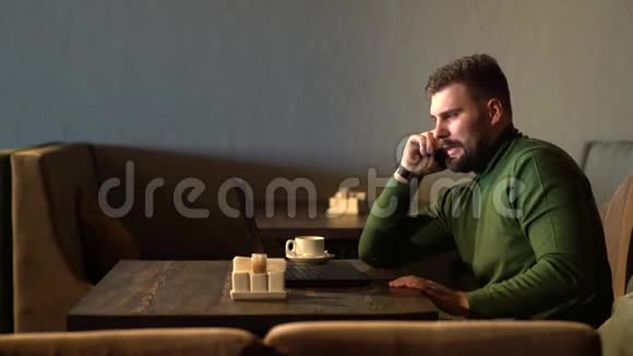 一个商人在咖啡馆里用手提电脑工作时一边说着电话视频的预览图