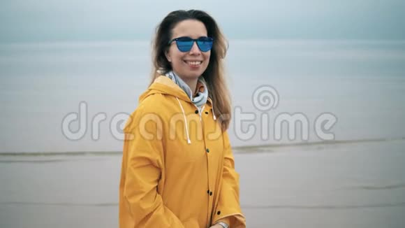 穿着黄色外套的微笑女士戴着太阳镜靠近大海背景是多云的天空视频的预览图