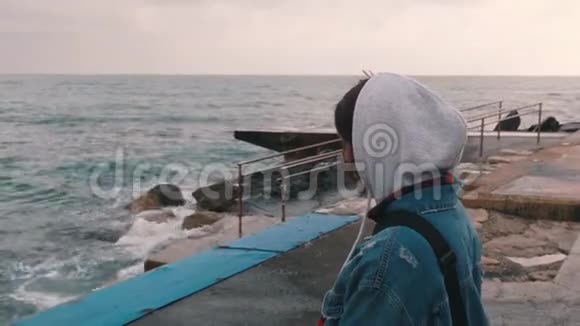 靠近码头的孤独女孩忧郁的女孩看着暴风雨的大海悲观的年轻女子穿着随意的风格视频的预览图