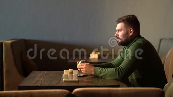 一个时髦男人坐在咖啡馆里用蓝牙耳机听音乐视频的预览图