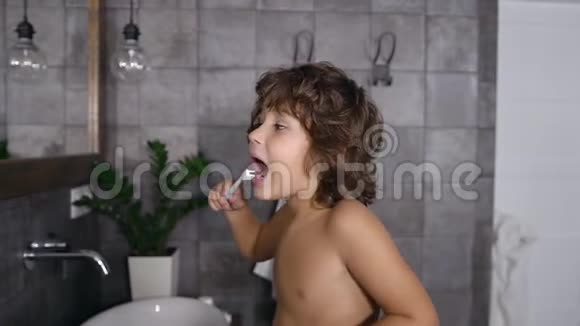 盥洗室里镜子旁的一个卷发小男孩在擦牙视频的预览图