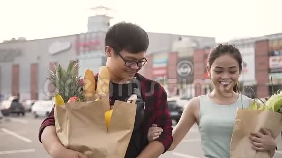 带着装满食物的纸袋在大型购物中心前缓慢行走的迷人微笑的男女视频的预览图