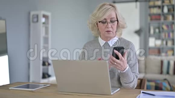 职业老妇人在手提电脑和智能电话上交谈视频的预览图