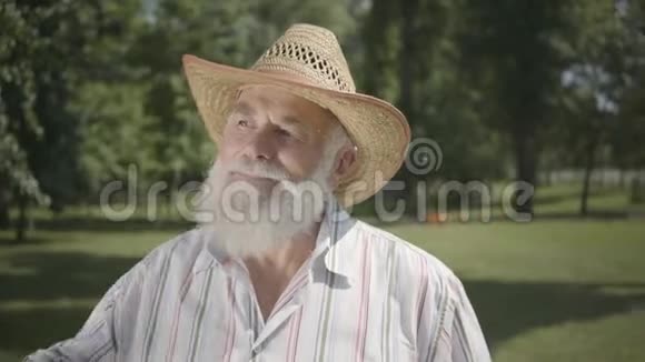 戴着草帽长着白胡子的自信老人微笑着挥舞着手站在公园视频的预览图