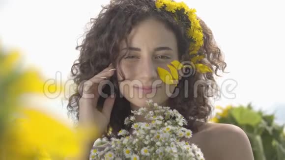 一个可爱的卷发女孩看着镜头微笑着站在向日葵花丛中的肖像视频的预览图