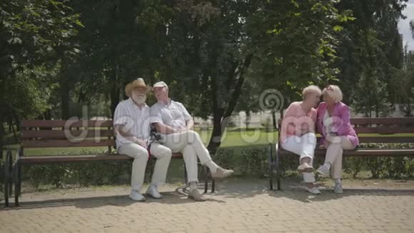 两对年长夫妇坐在夏季公园里彼此靠近的长凳上成熟的人在户外休息快乐视频的预览图