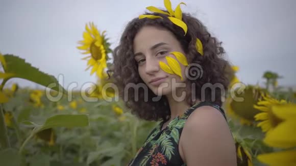 美丽的卷曲女孩的肖像邀请吸引观众在向日葵领域明亮的黄色连接视频的预览图