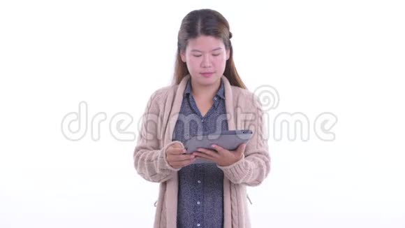 快乐的年轻亚洲女人一边思考一边用数字平板电脑准备过冬视频的预览图