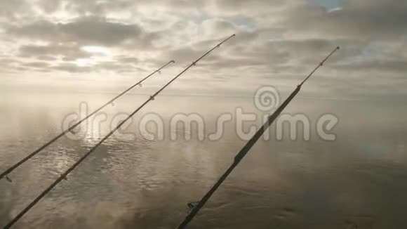 三根鱼竿在水面上的景色钓船上挂着尖嘴多云的天空在背景上视频的预览图