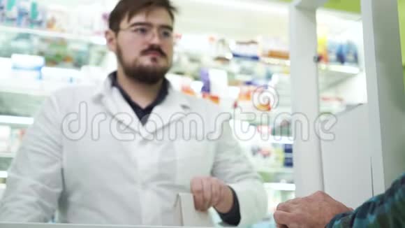 年轻的胡子药剂师给顾客送白色包裹和药物穿白色长袍的专业工人视频的预览图
