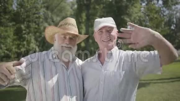 两个英俊的老人在公园里挥舞着手看着镜头户外休闲成熟的人在休息视频的预览图